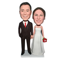 Groom in black suit and bride in white wedding dress handing a flower bobblehead