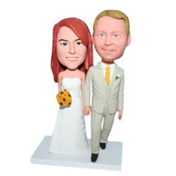 Groom in beige suit and bride in white wedding dress handing with a bunch of flowers bobblehead